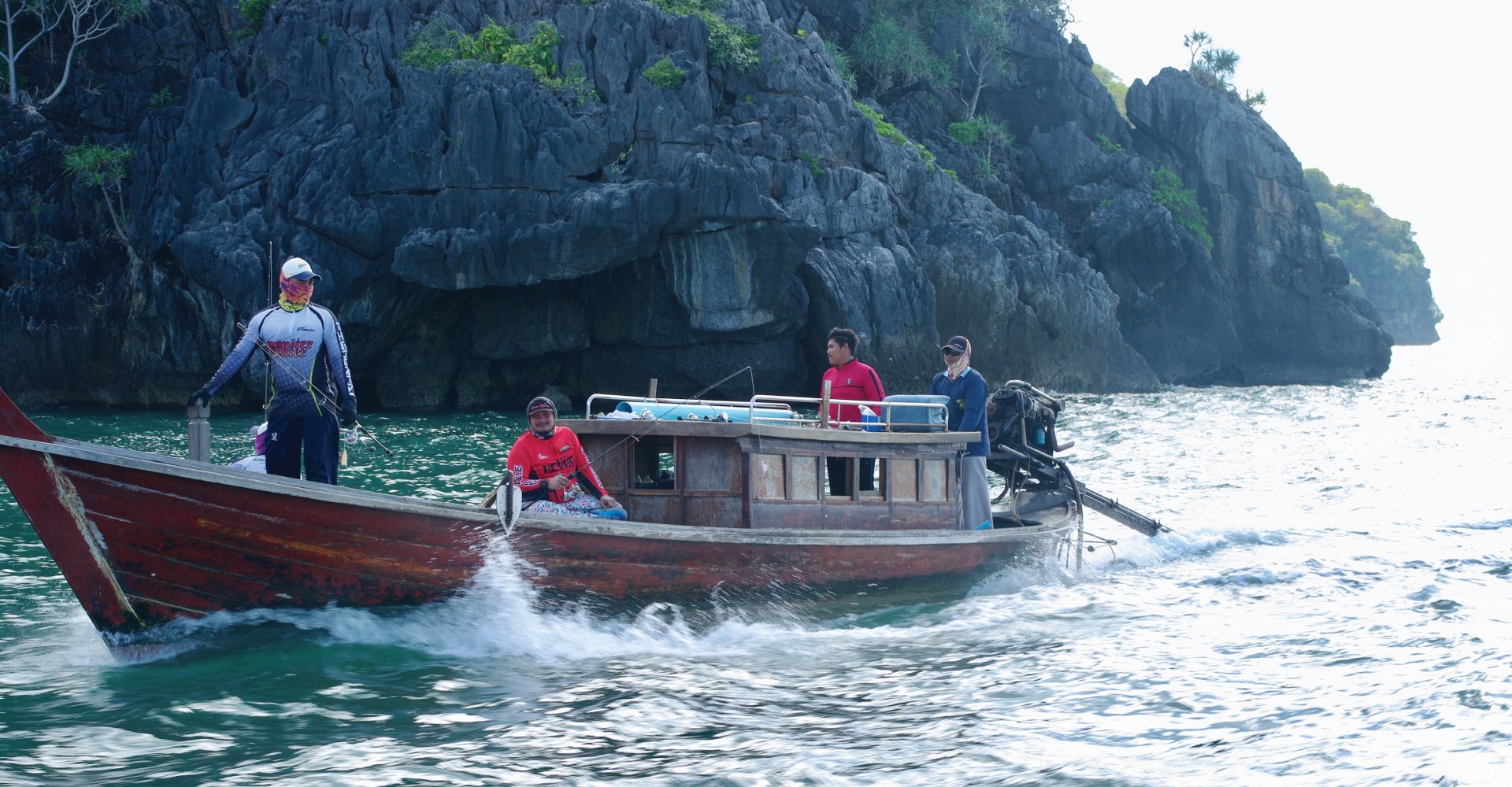 Traditional long-tail boat travelling beside limestone cliffs near Koh Bulon-Lae